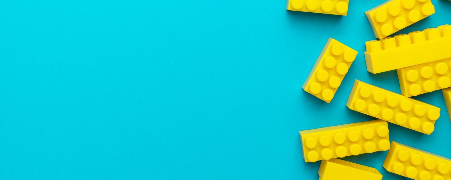 Yellow Plastic Building Blocks On Turquoise Blue Background With Copy Space